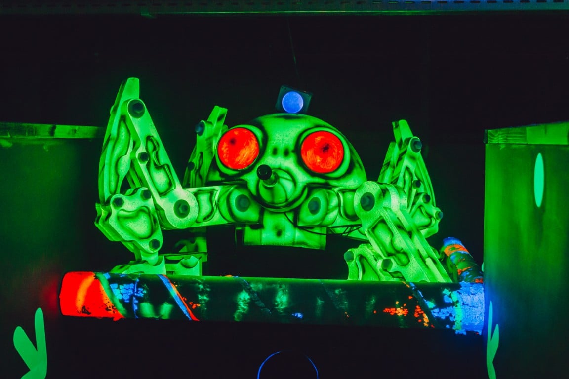 Een groene robotspin met rode ogen in de lasershoot-arena